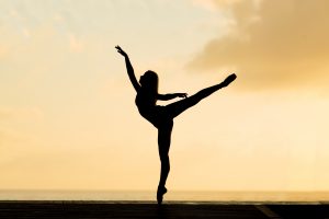 person holding a ballet pose in front of a warm yellow sunrise