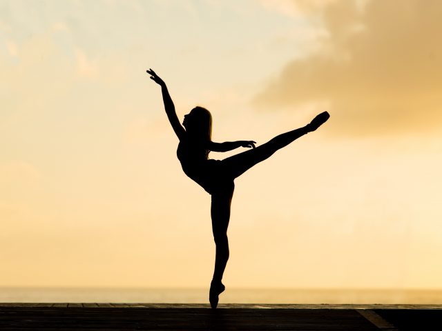 person holding a ballet pose in front of a warm yellow sunrise