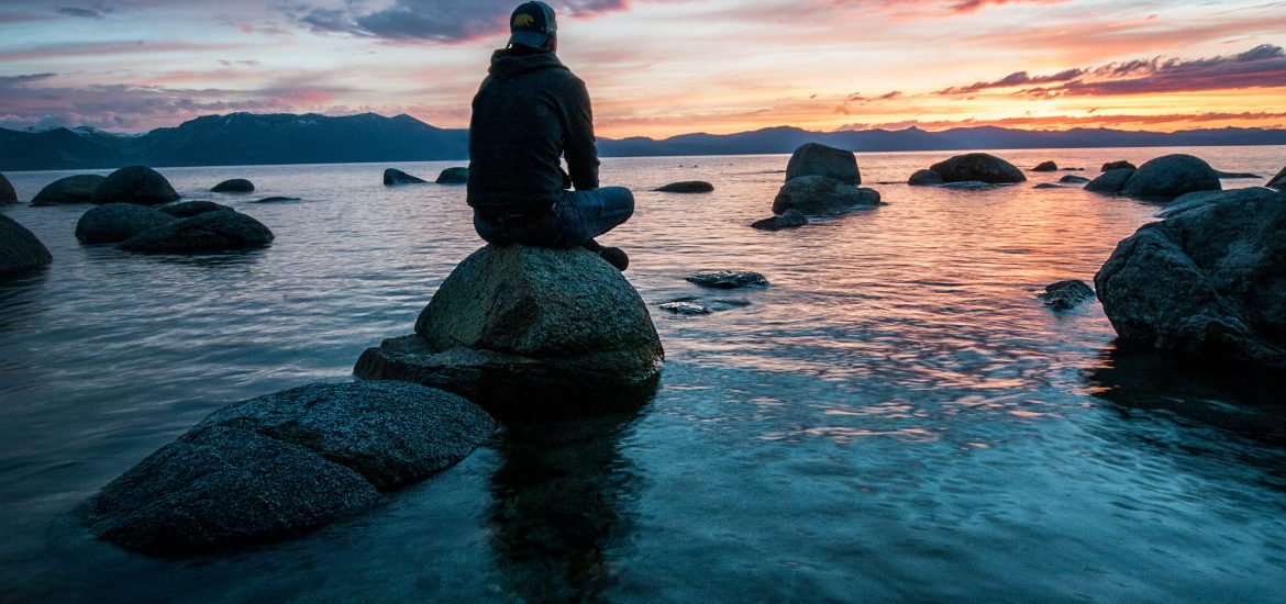 man sitting on rock overlooking sunset