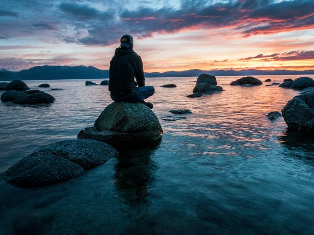 man sitting on rock overlooking sunset
